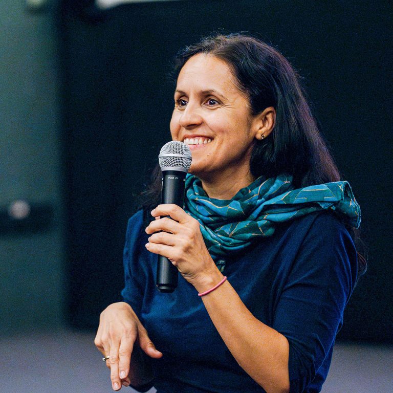 Ligia Soare, smiling and speaking into a handheld microphone, wearing a navy top and teal scarf. Photo: Tóth Helga.